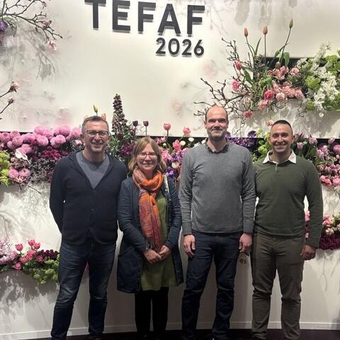 One woman and three men stand before a wall that says TEFAF 2026 on it and is decorated with flowers